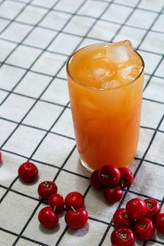Refreshing iced tropical fruit juice with vibrant red acerola cherries on a checkered cloth, perfect for summer.