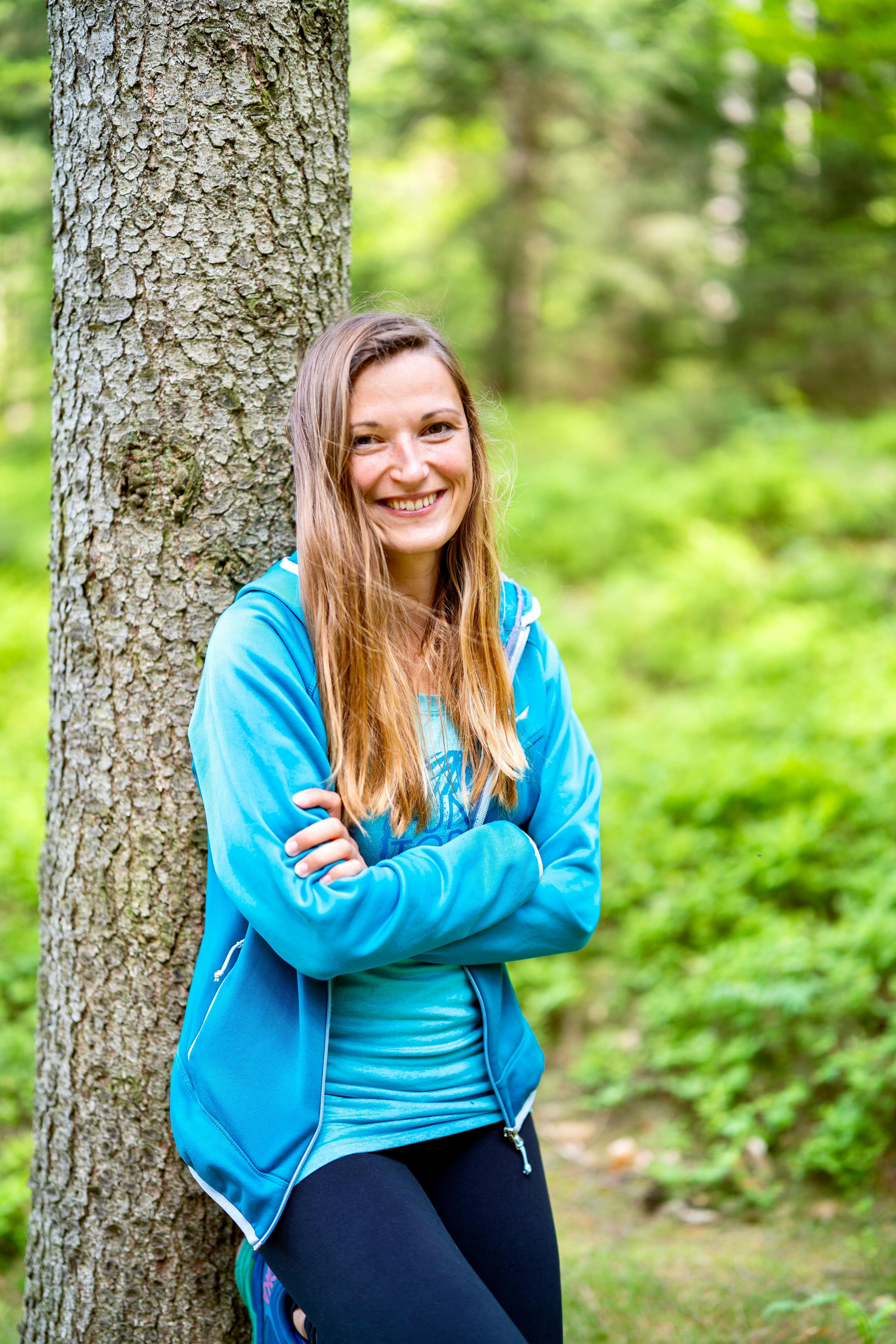 Cheerful woman leans against a tree in a vibrant forest in Jonsdorf, Germany.