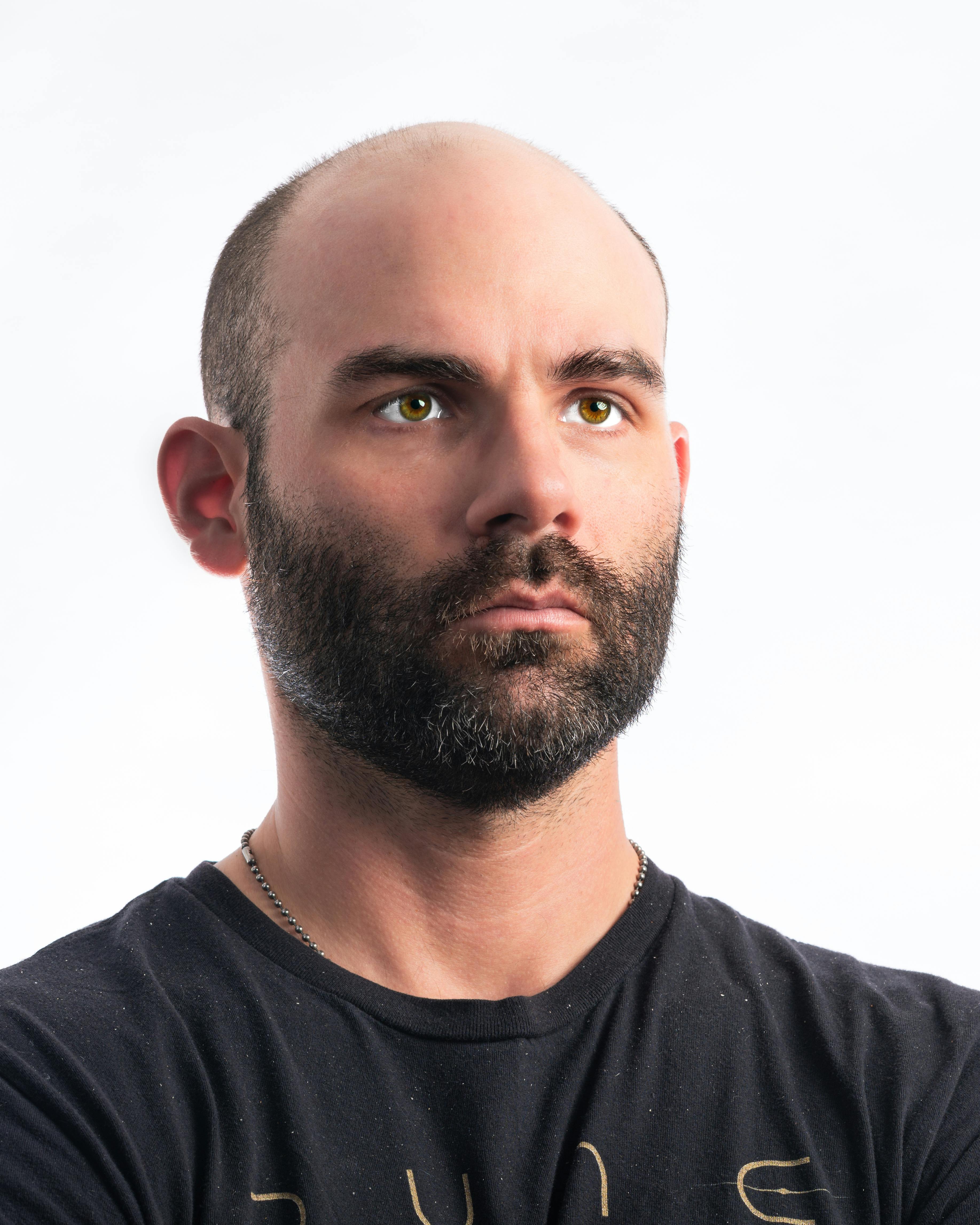 Close-up portrait of a bearded man with a focused expression against a white background.