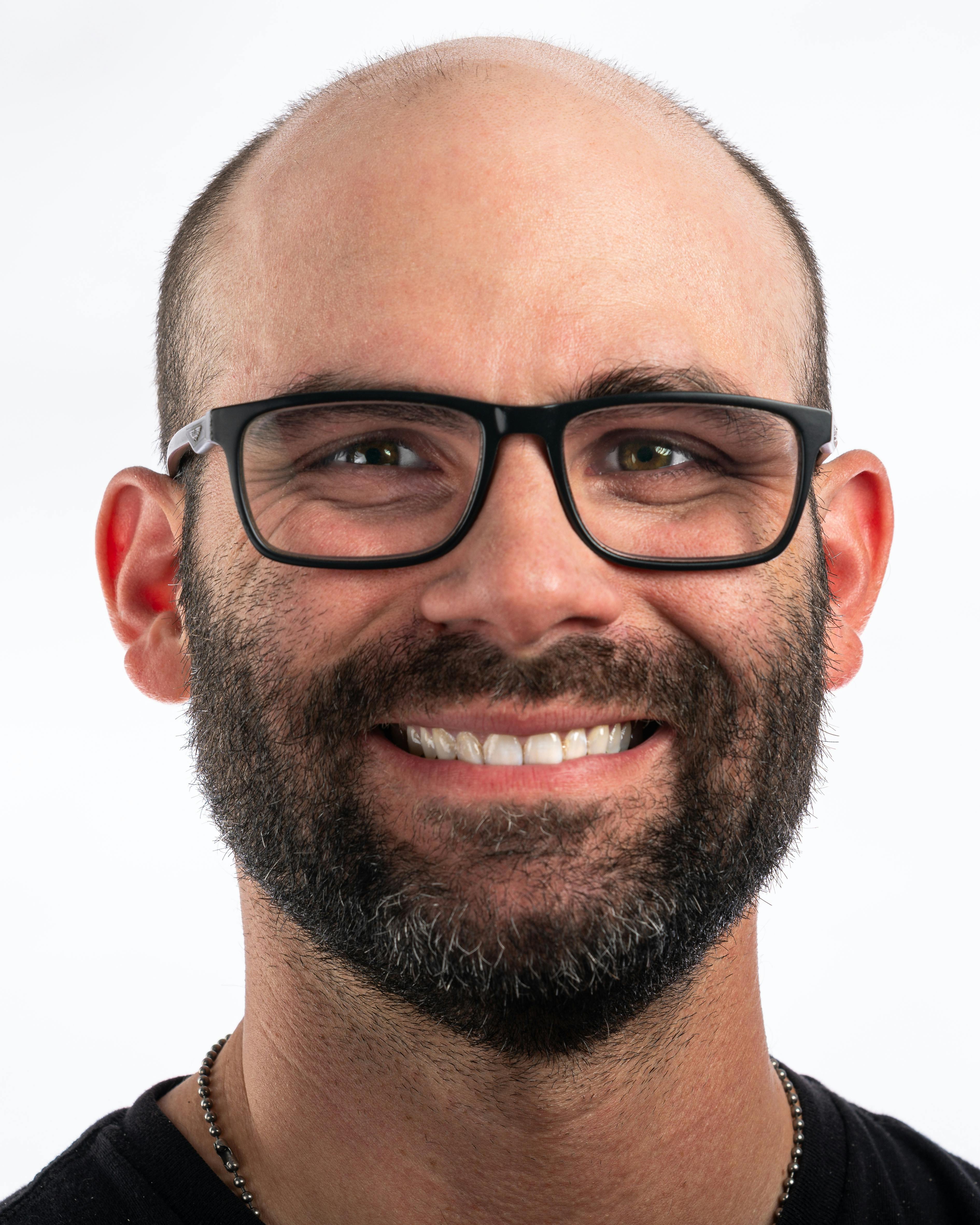 Portrait of a bald man with glasses smiling against a white background.