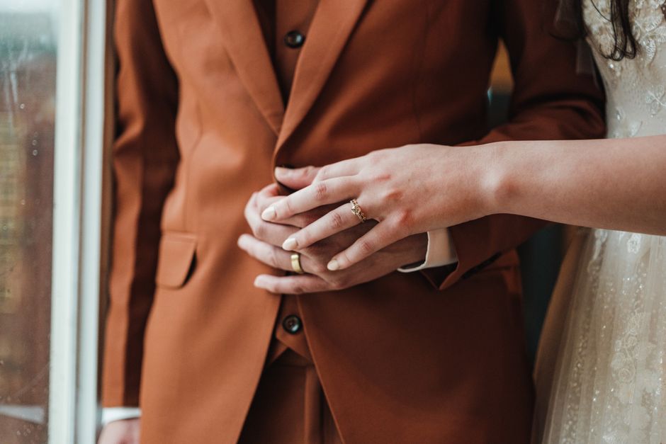 Intimate detail of a couple's hands with wedding rings, showcasing elegant attire and romantic ambiance.