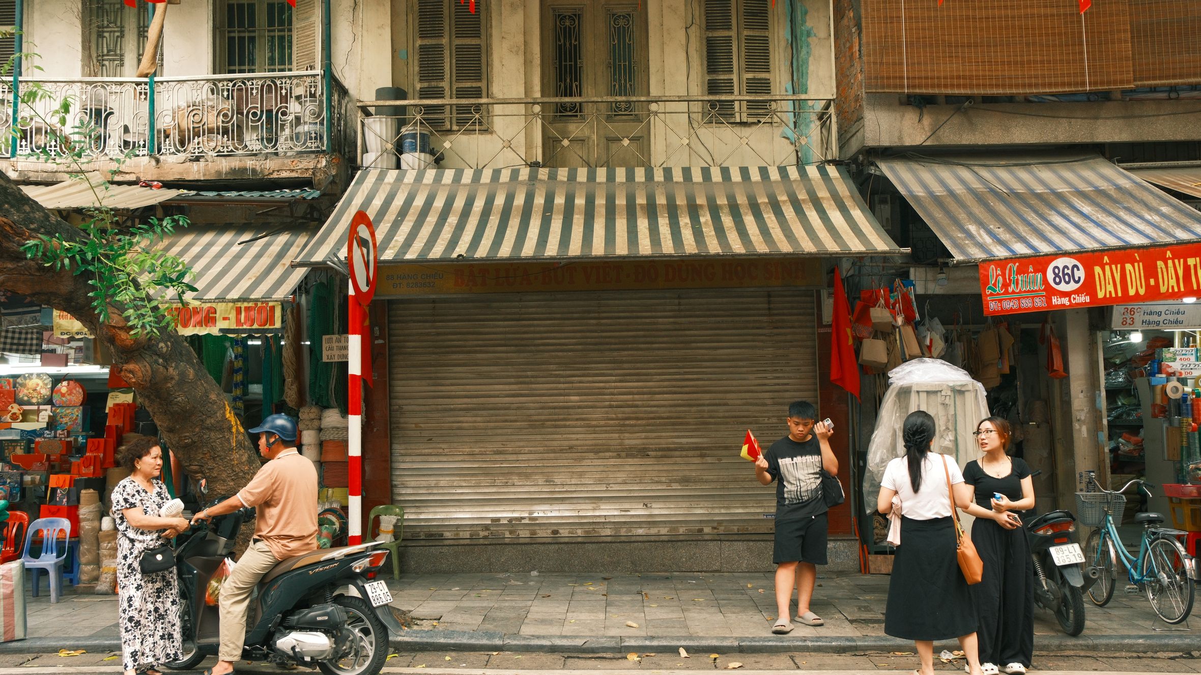 A lively street scene in Hanoi, Vietnam featuring people interacting on a bustling sidewalk.