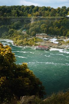 Scenic autumn view of the Niagara River with lush greenery and tour boats.