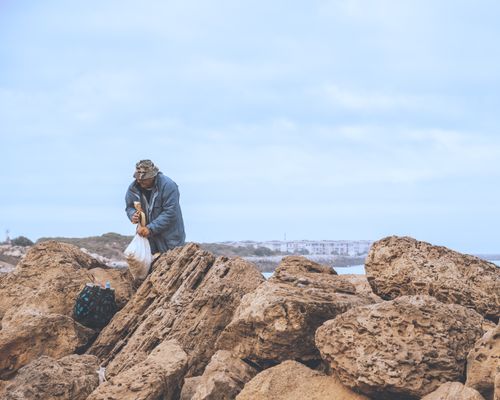 Free An adult male is seen collecting items by rocky seaside terrain on a cloudy day. Stock Photo