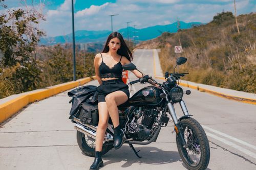 Free A stylish woman in black attire poses on a motorcycle outdoors with a scenic mountain view. Stock Photo