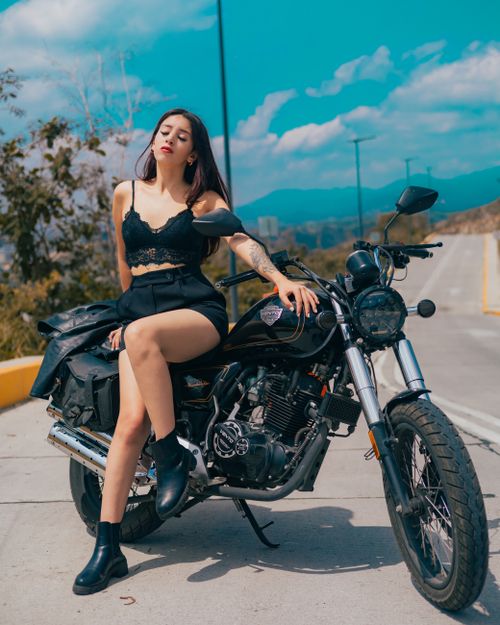 Free A confident woman poses on a motorcycle on a sunny day, exemplifying freedom and adventure. Stock Photo