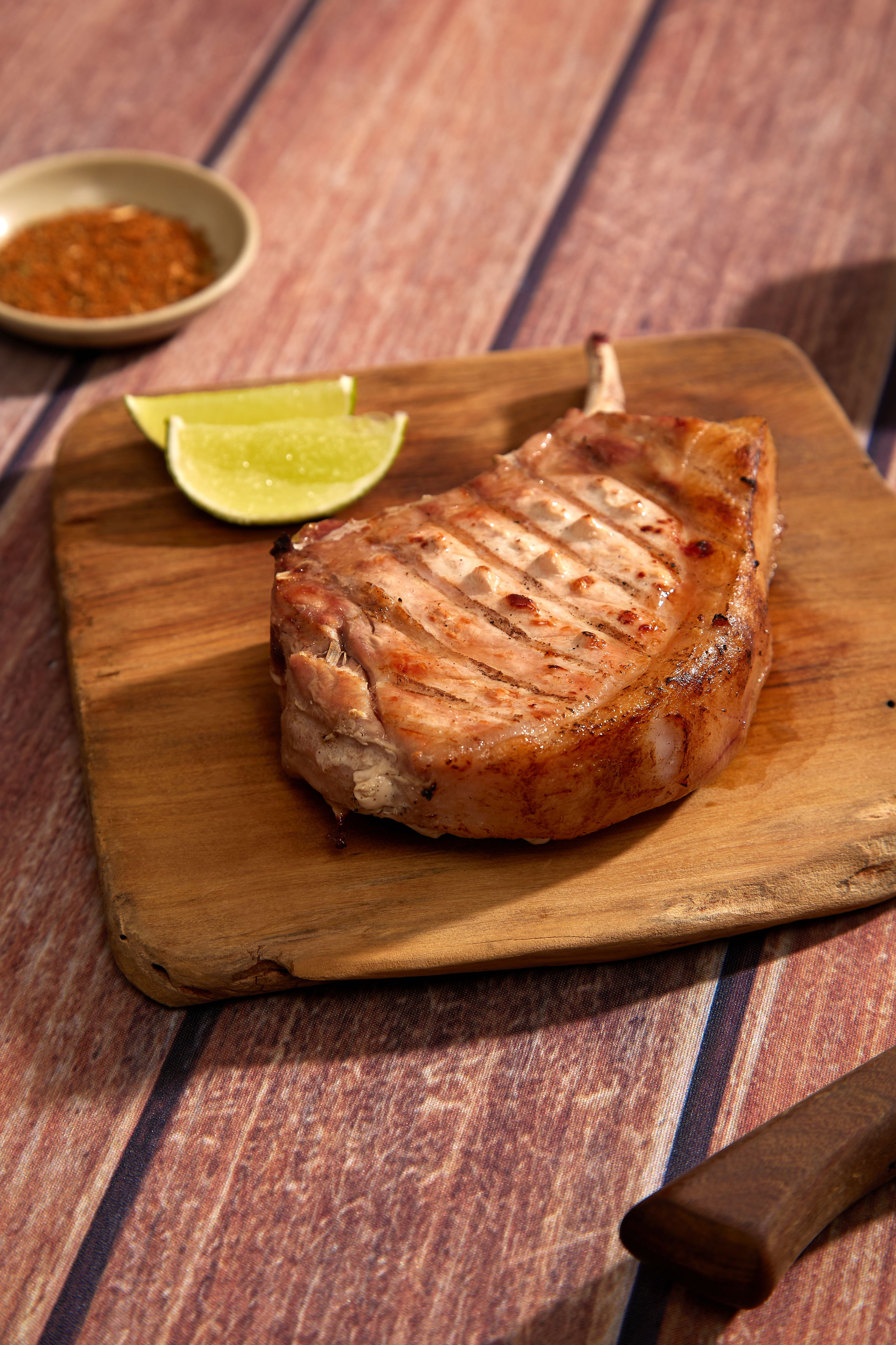 Delicious grilled pork chop served with lime slices on a wooden board.