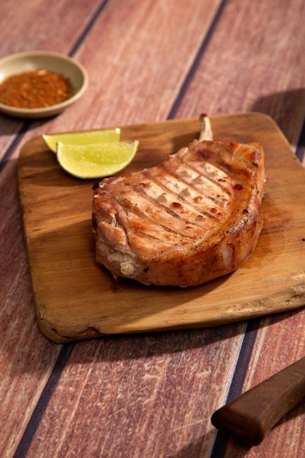 Two thick bone-in pork chops in a cast iron skillet, deeply browned and basted with melted butter, garlic cloves, and sprigs of thyme.