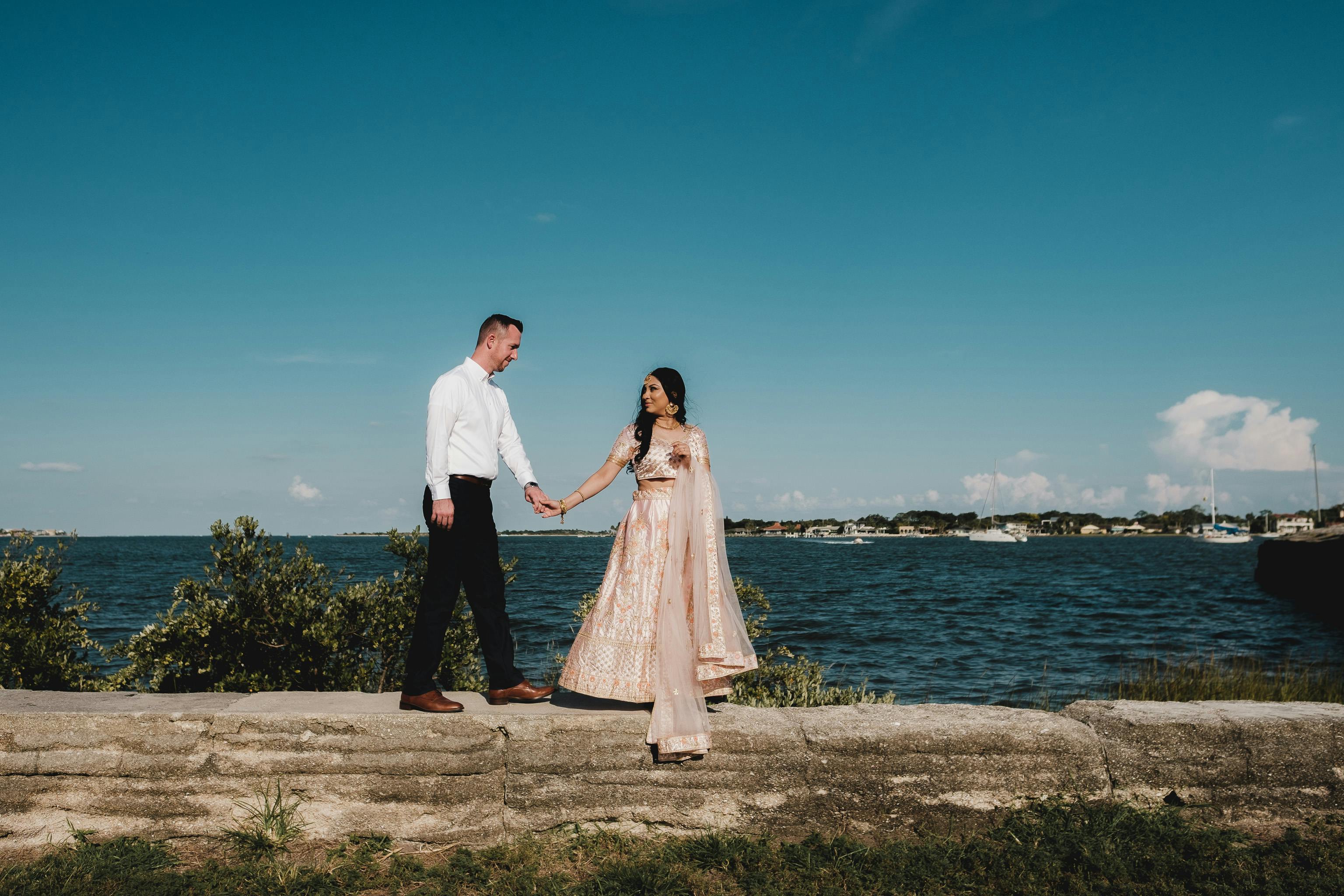 A couple holding hands by the ocean, blending traditional and modern fashion.