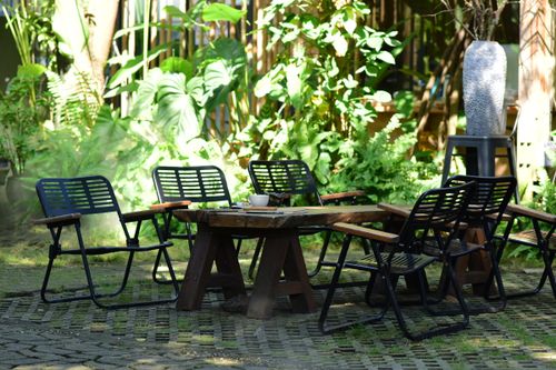 Free Charming outdoor seating area with chairs and a rustic table surrounded by lush greenery. Stock Photo