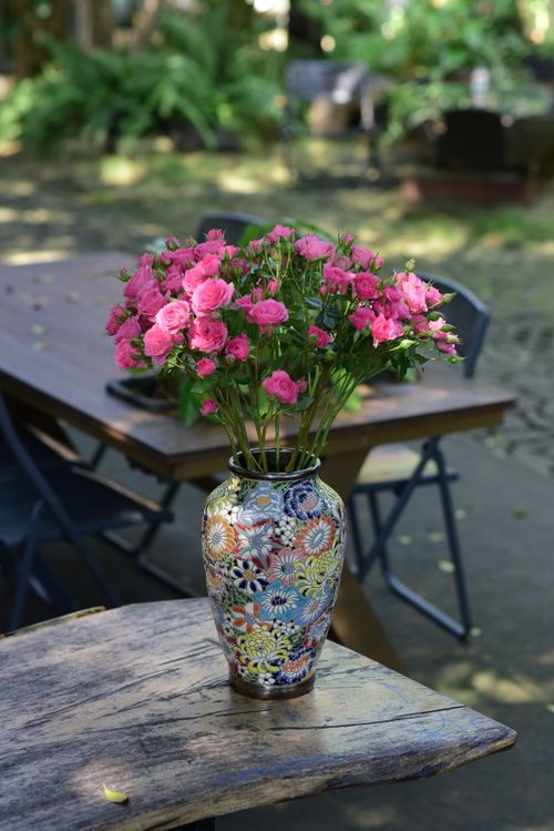 Free A beautiful arrangement of pink flowers in a colorful vase on a wooden table outdoors. Stock Photo