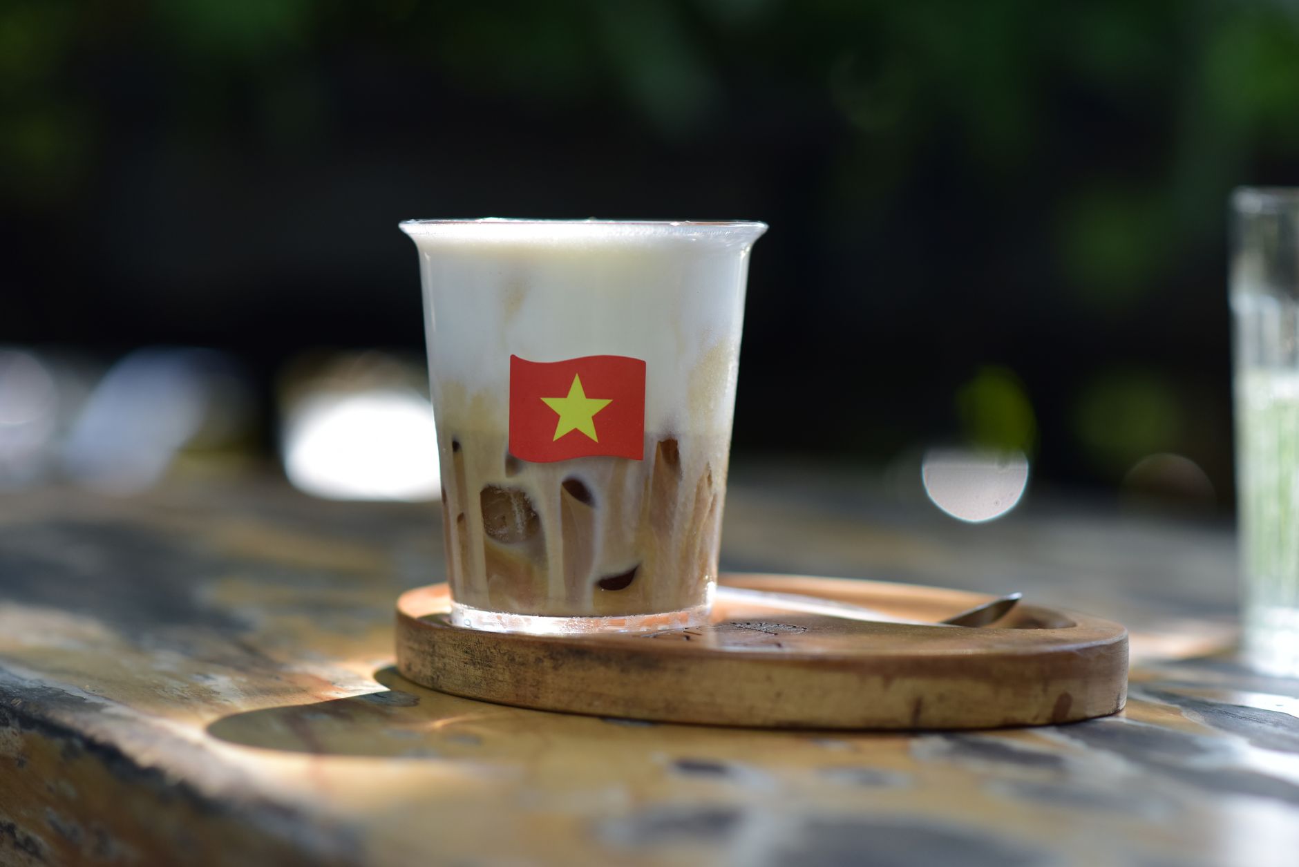 A creamy Vietnamese iced coffee with a flag emblem magnified by sunlight on a wooden table, perfect for a summer refreshment.