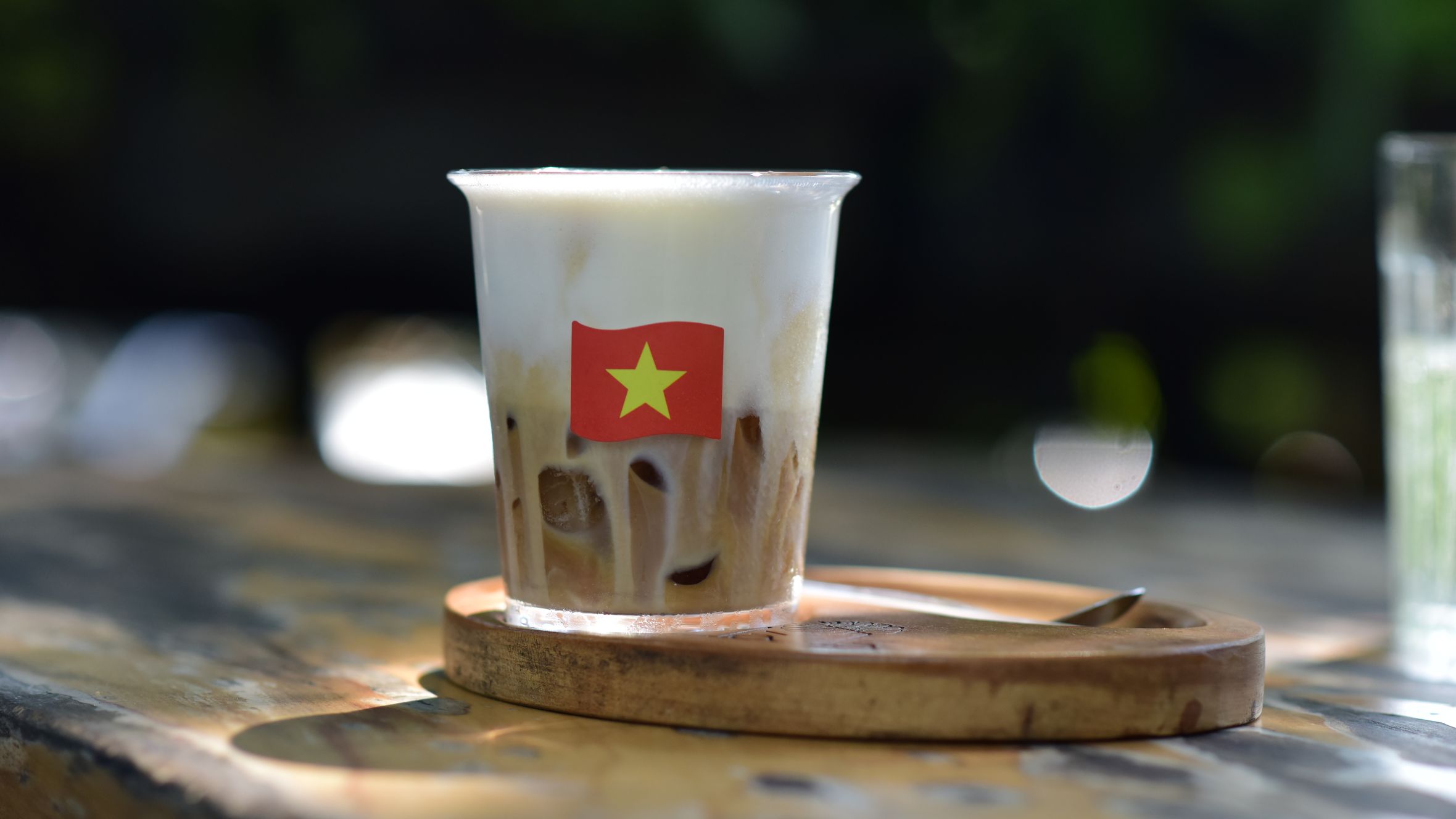A creamy Vietnamese iced coffee with a flag emblem magnified by sunlight on a wooden table, perfect for a summer refreshment.