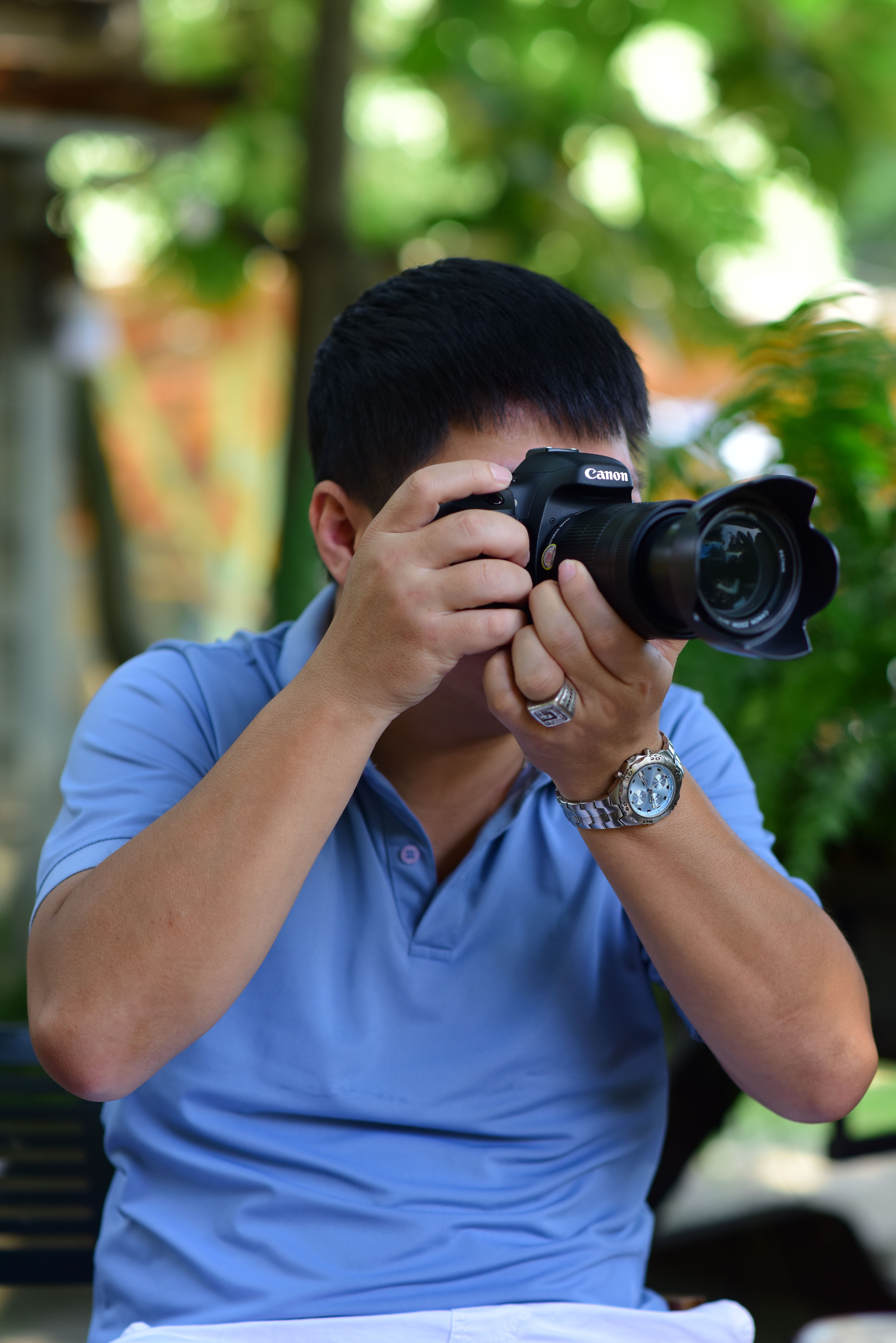 Adult male photographer capturing outdoors in casual blue polo shirt.