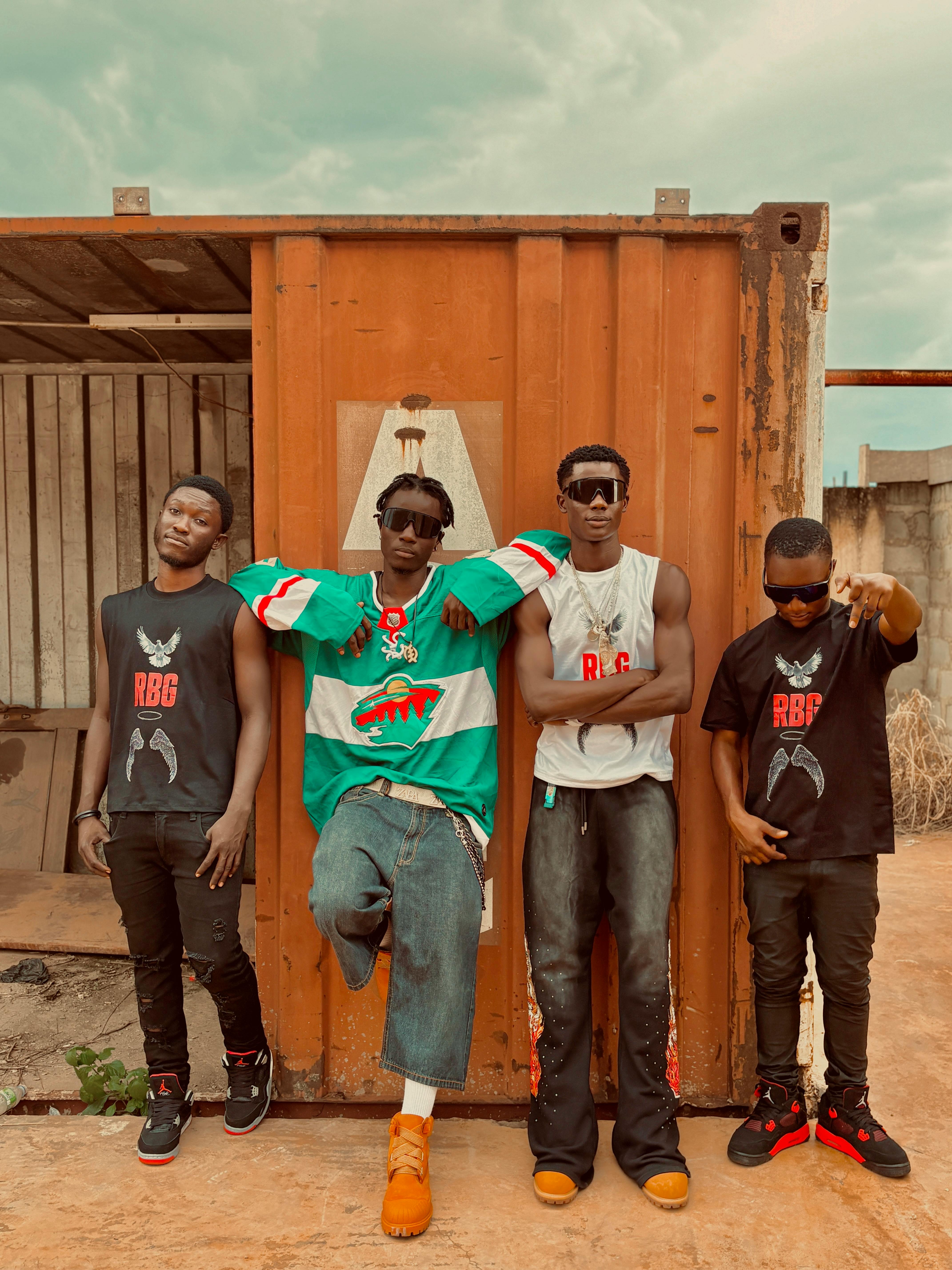 Four individuals in stylish urban streetwear pose confidently in front of an industrial backdrop.