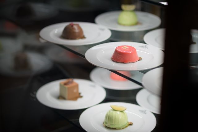 A variety of colorful desserts elegantly presented on white plates in a display case.
