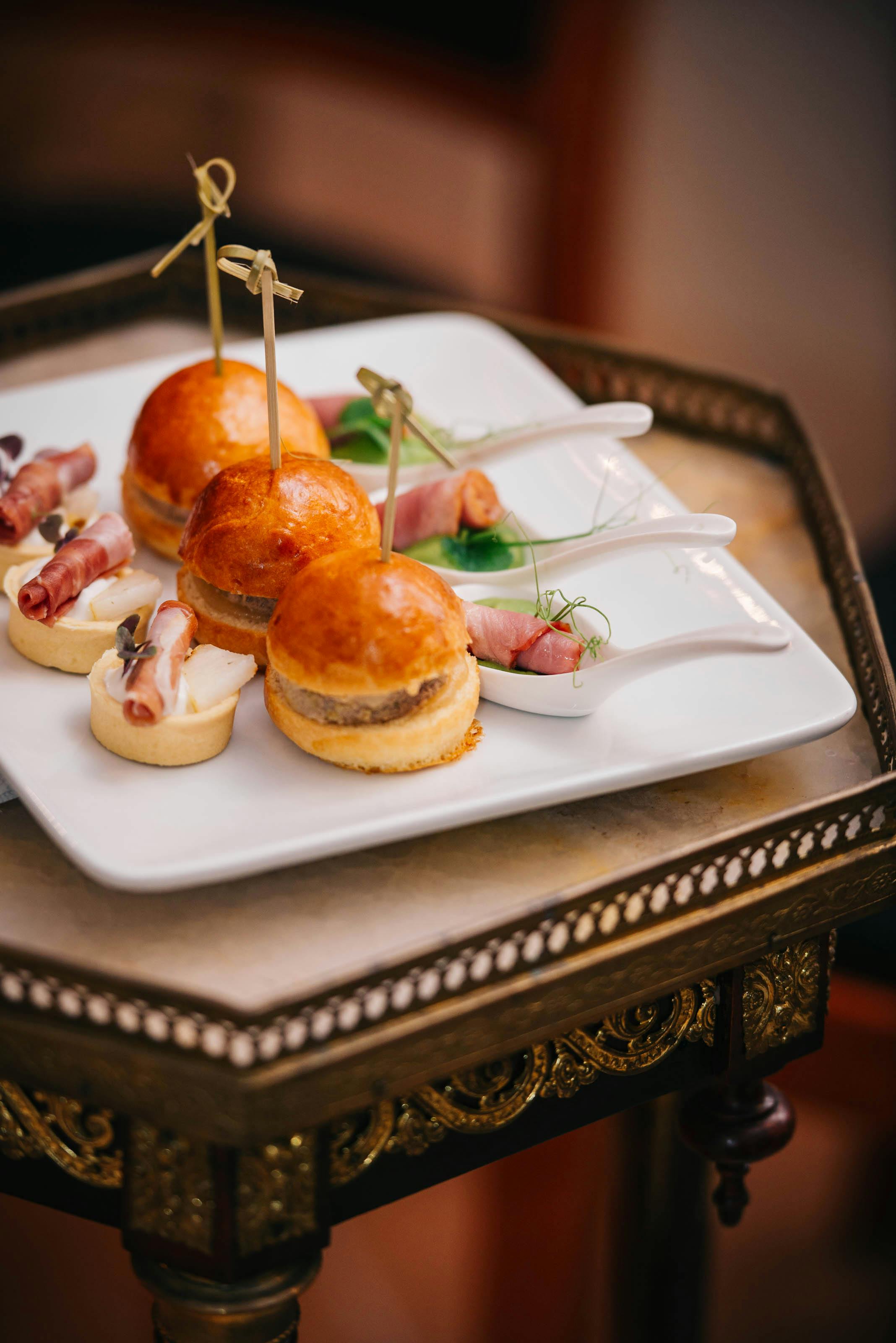 Gourmet slider burgers and bacon appetizers elegantly presented on a white platter.