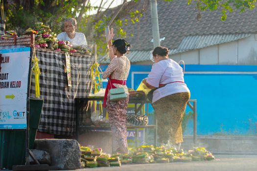 Balinese women in traditional attire preparing offerings at a Denpasar market during a sunny day.