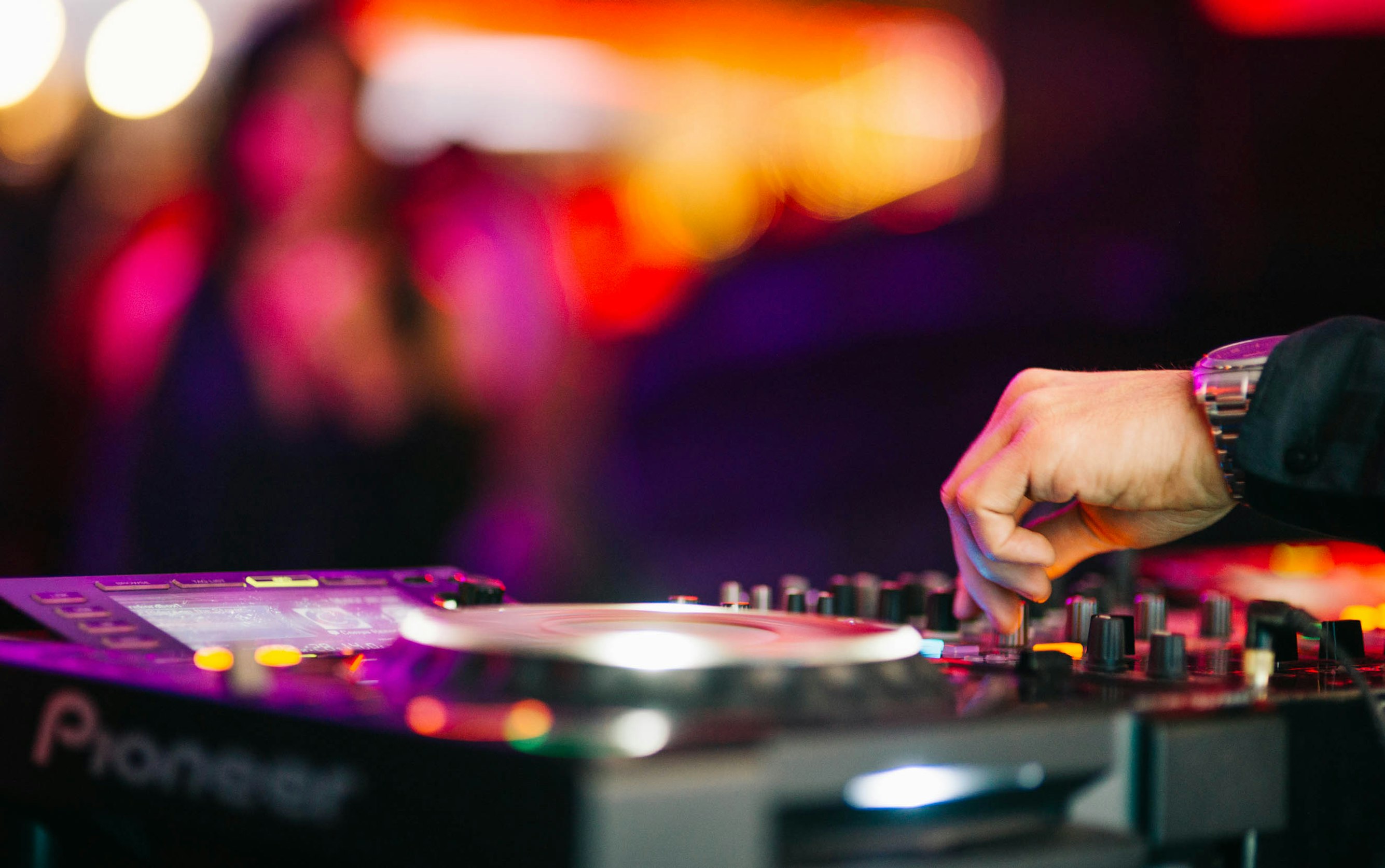 A DJ's hands on a mixer at a vibrant party