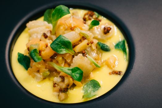 Elegant gourmet dish with vegetables served on a vibrant yellow sauce, garnished with fresh greens.