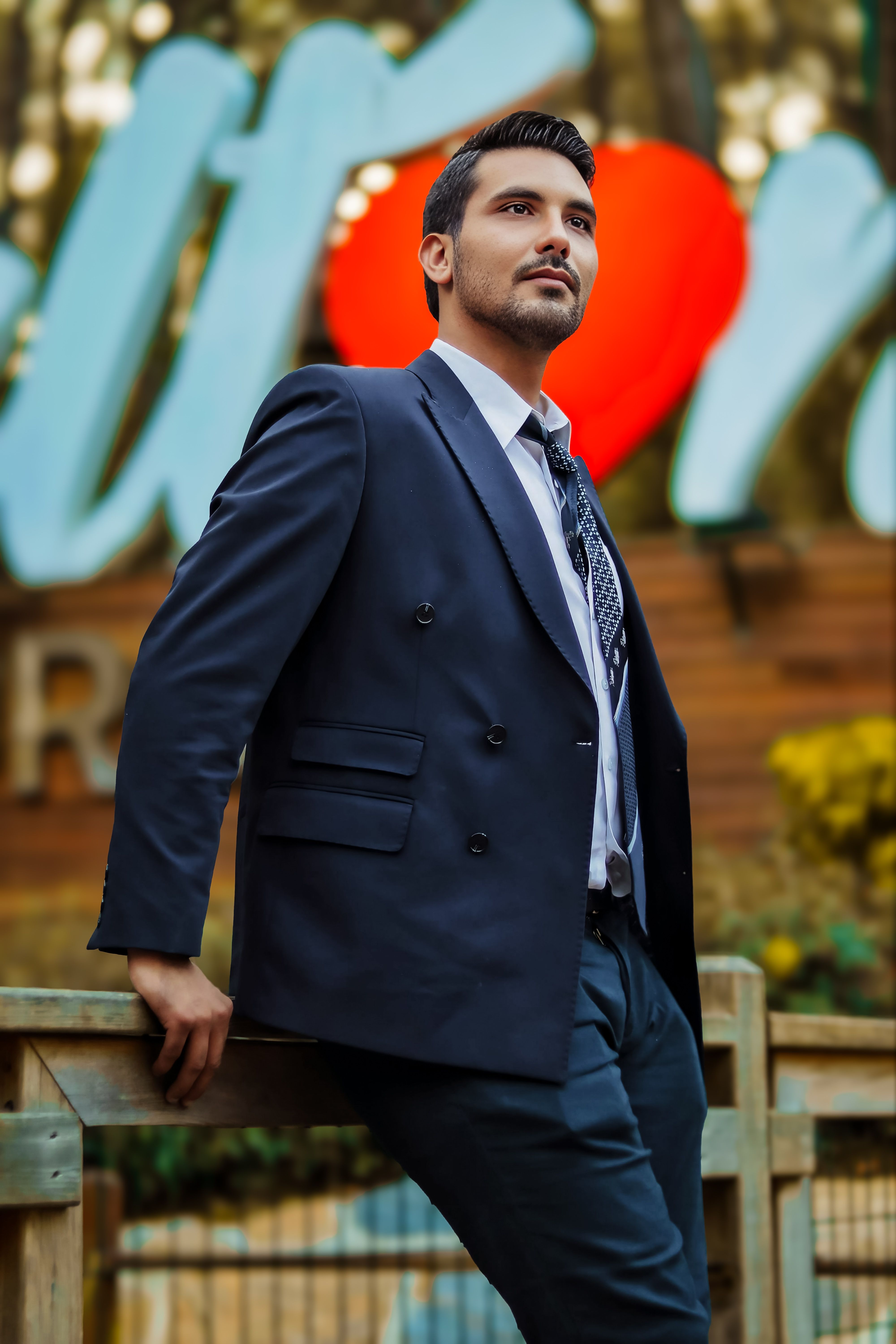 Stylish man in a suit posing outdoors with vibrant blurred signage backdrop.