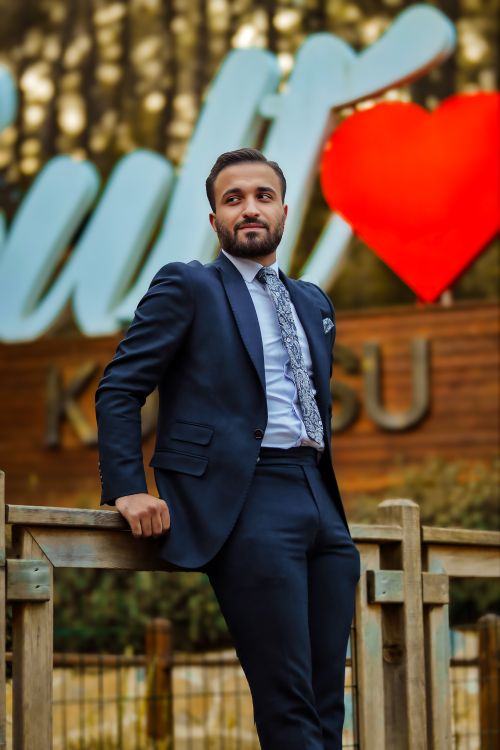 Free Man in formal suit poses outdoors beside a large heart sign, exuding confidence. Stock Photo