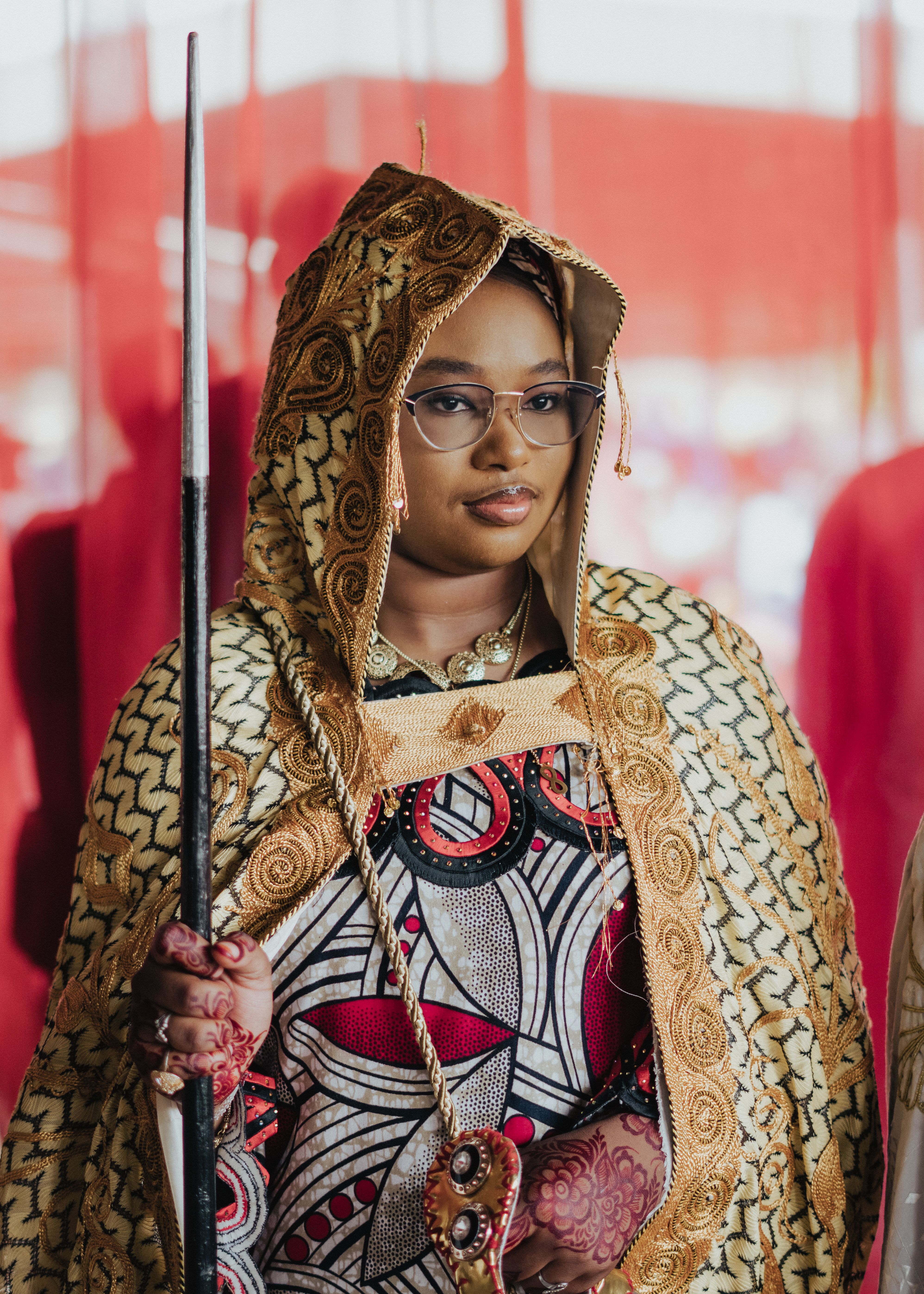 A woman in intricate African cultural attire holding a ceremonial staff.