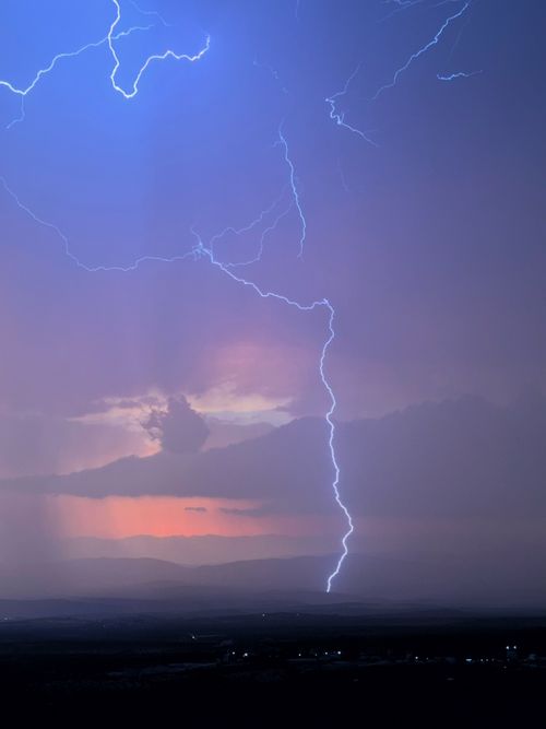 Free A striking lightning bolt illuminates a moody sky over mountains at dusk. Stock Photo