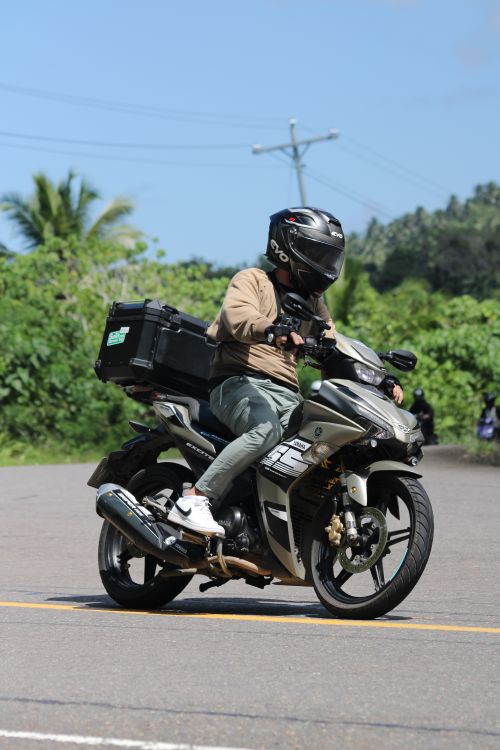 Free A motorcyclist in gear rides on a road surrounded by greenery under a clear sky. Stock Photo