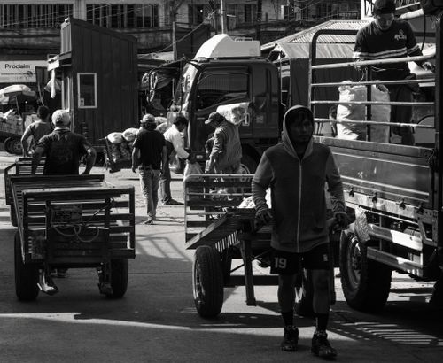 Free A lively black and white market scene with porters, carts, and trucks during the day. Stock Photo