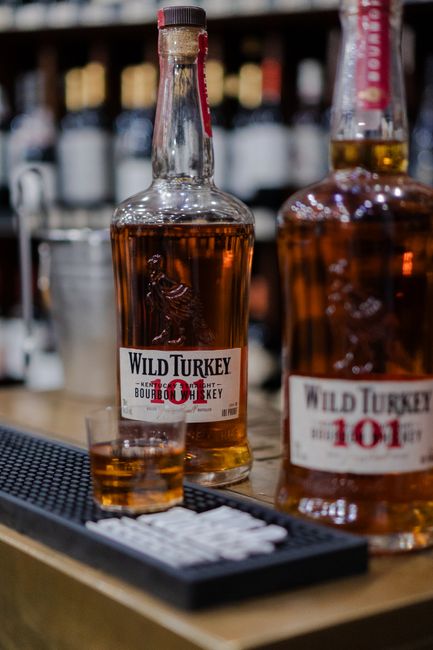 A glass of amber bourbon on the rocks next to an open bottle, showing the whiskey's deep caramel color.