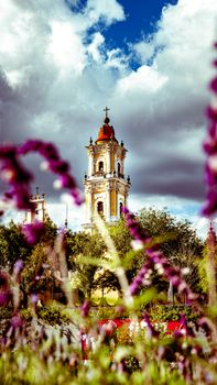 A picturesque view of a historic church tower with colorful flowers in the foreground under a dramatic sky.