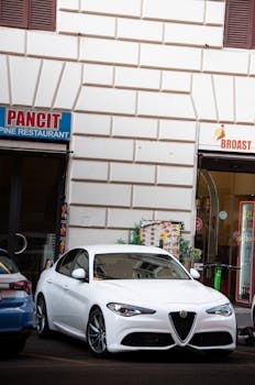 White Alfa Romeo sedan parked outside restaurants in a metropolitan area, showcasing luxury and style.