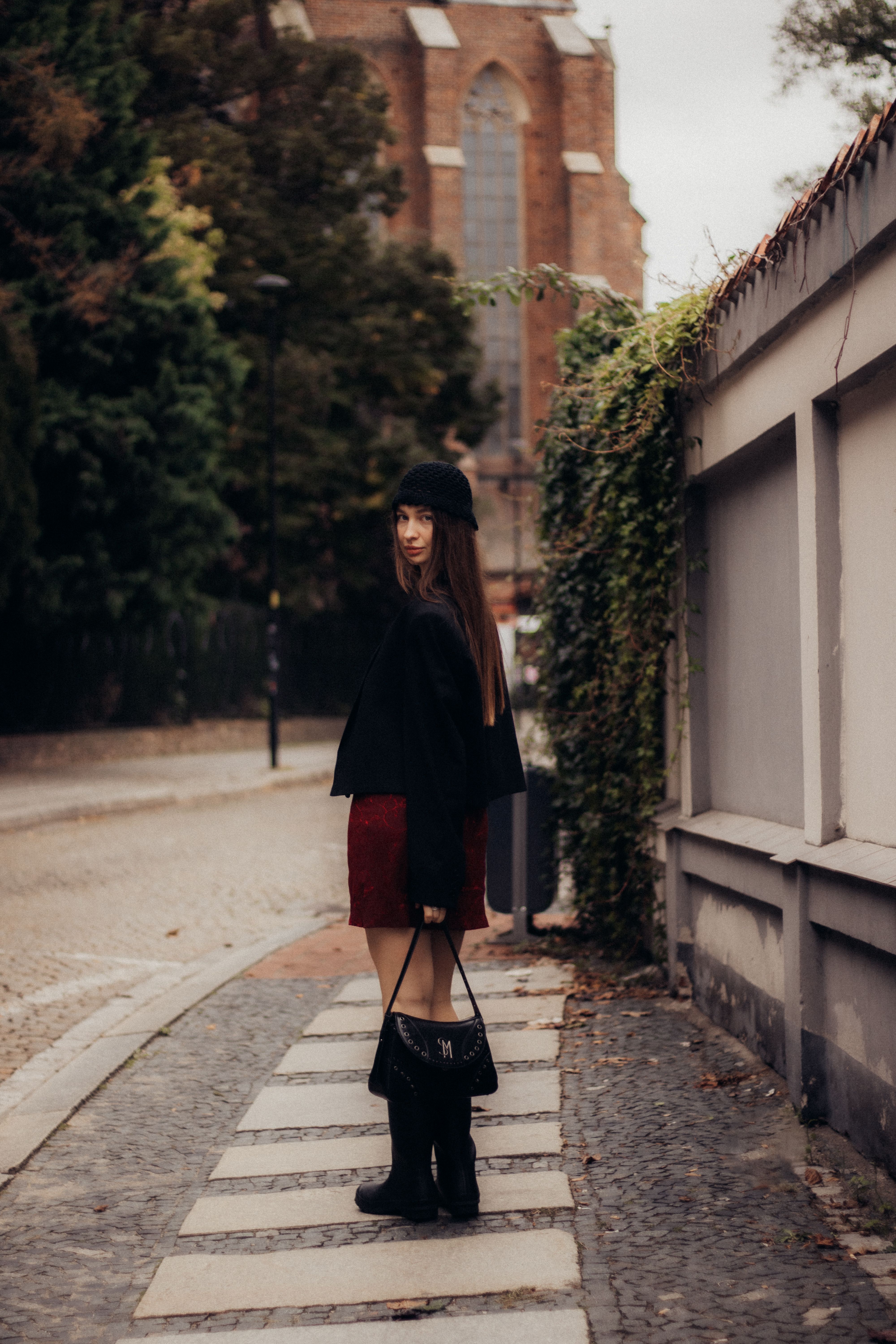 Young woman in fall fashion walking near historic European church on a cobblestone street.