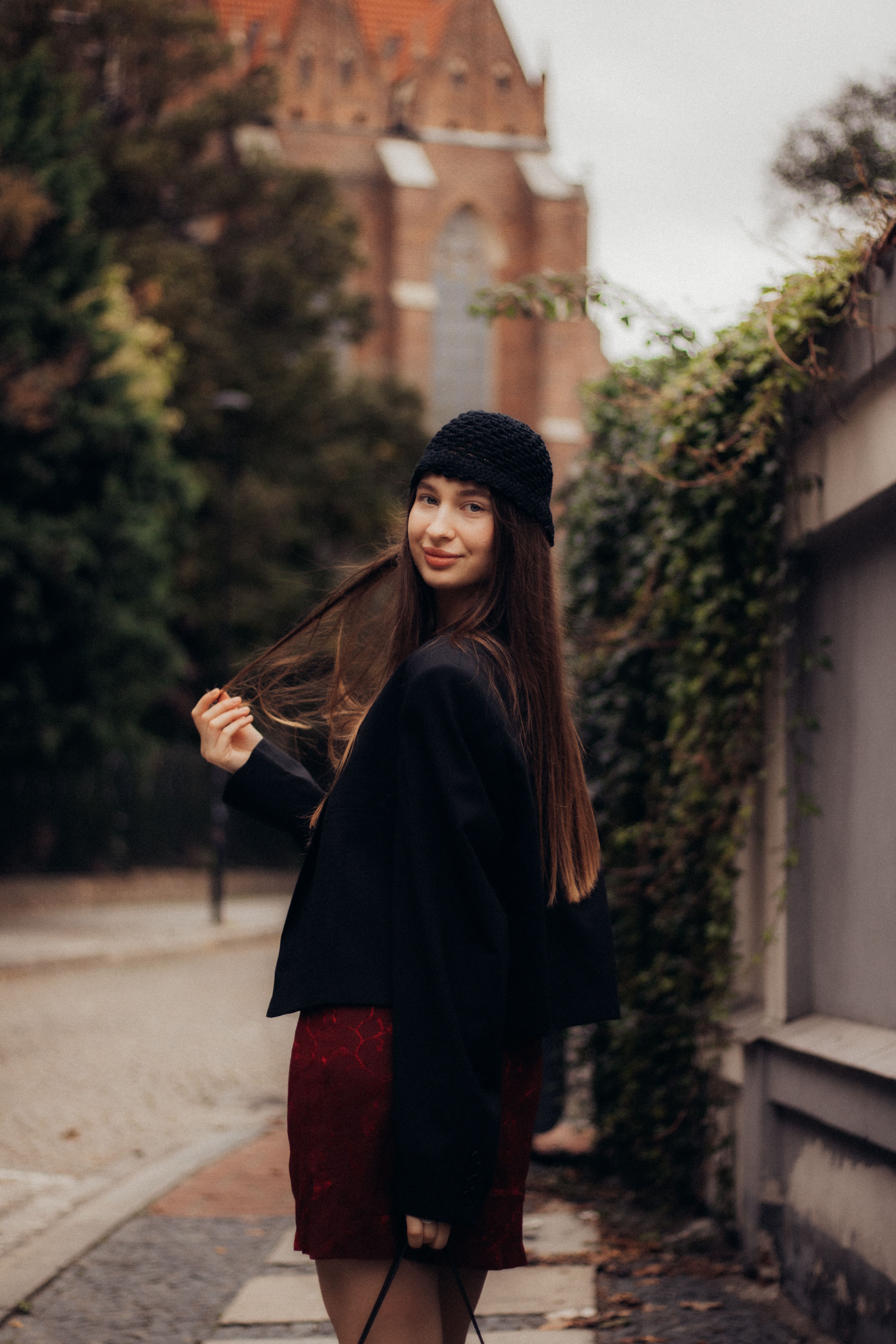 Woman in autumn attire walking down a city street with ivy-covered walls.