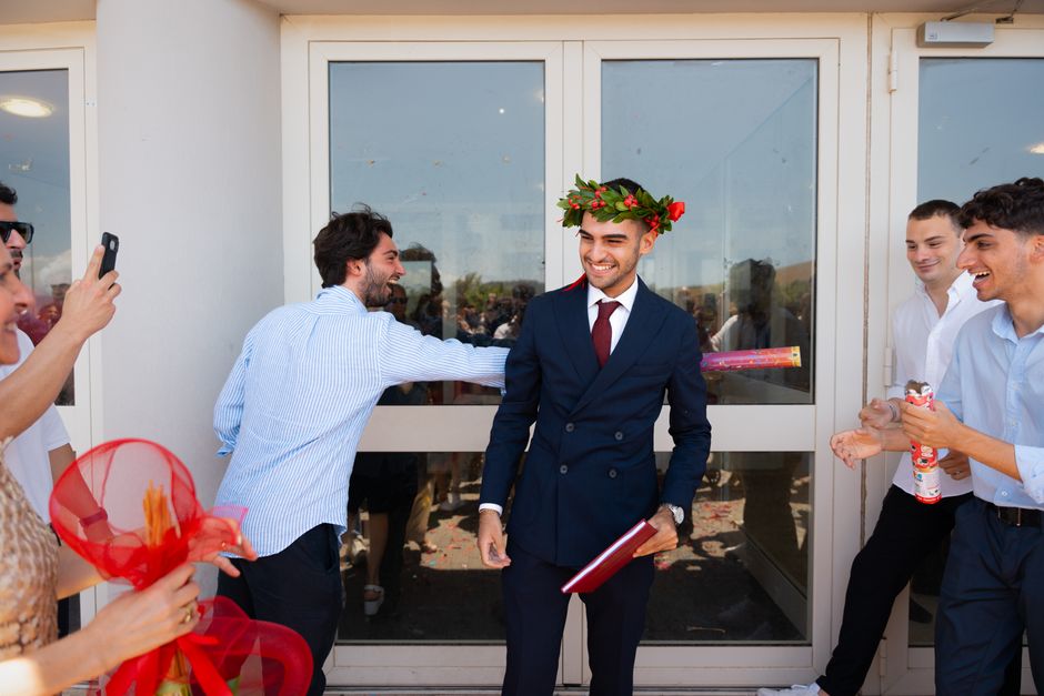 Cheerful graduate celebrating with friends outdoors, wearing a laurel wreath.