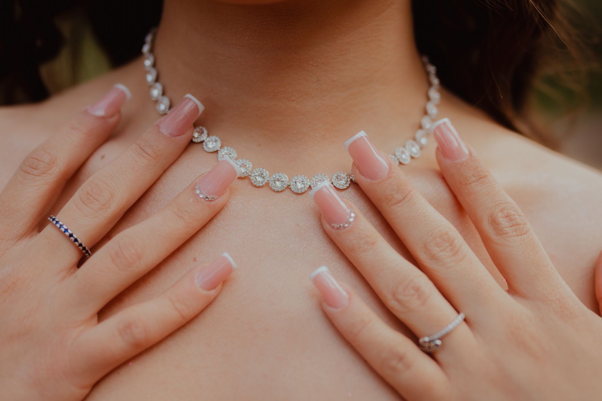 Close-up of elegant diamond necklace and manicured hands, showcasing jewelry fashion and style.