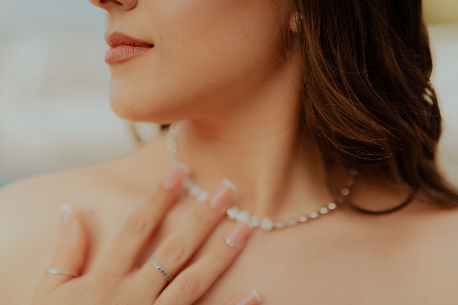 Close-up of a woman touching her neck and sparkling necklace in warm directional light.