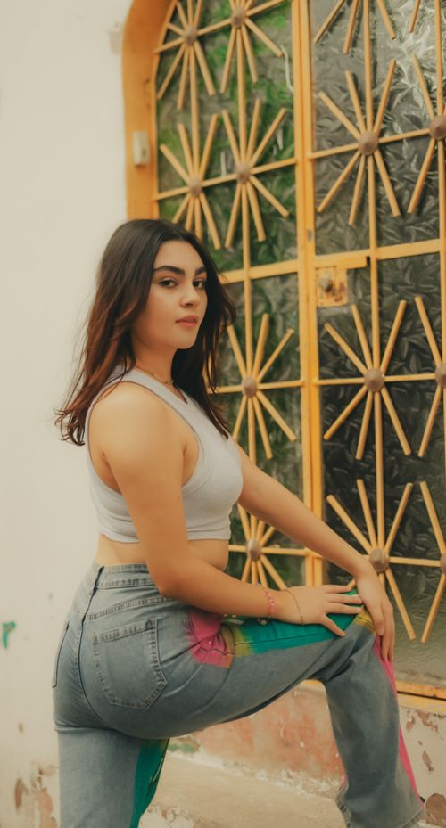 Free A young woman posing confidently outside an artistic window with geometric ornaments. Stock Photo