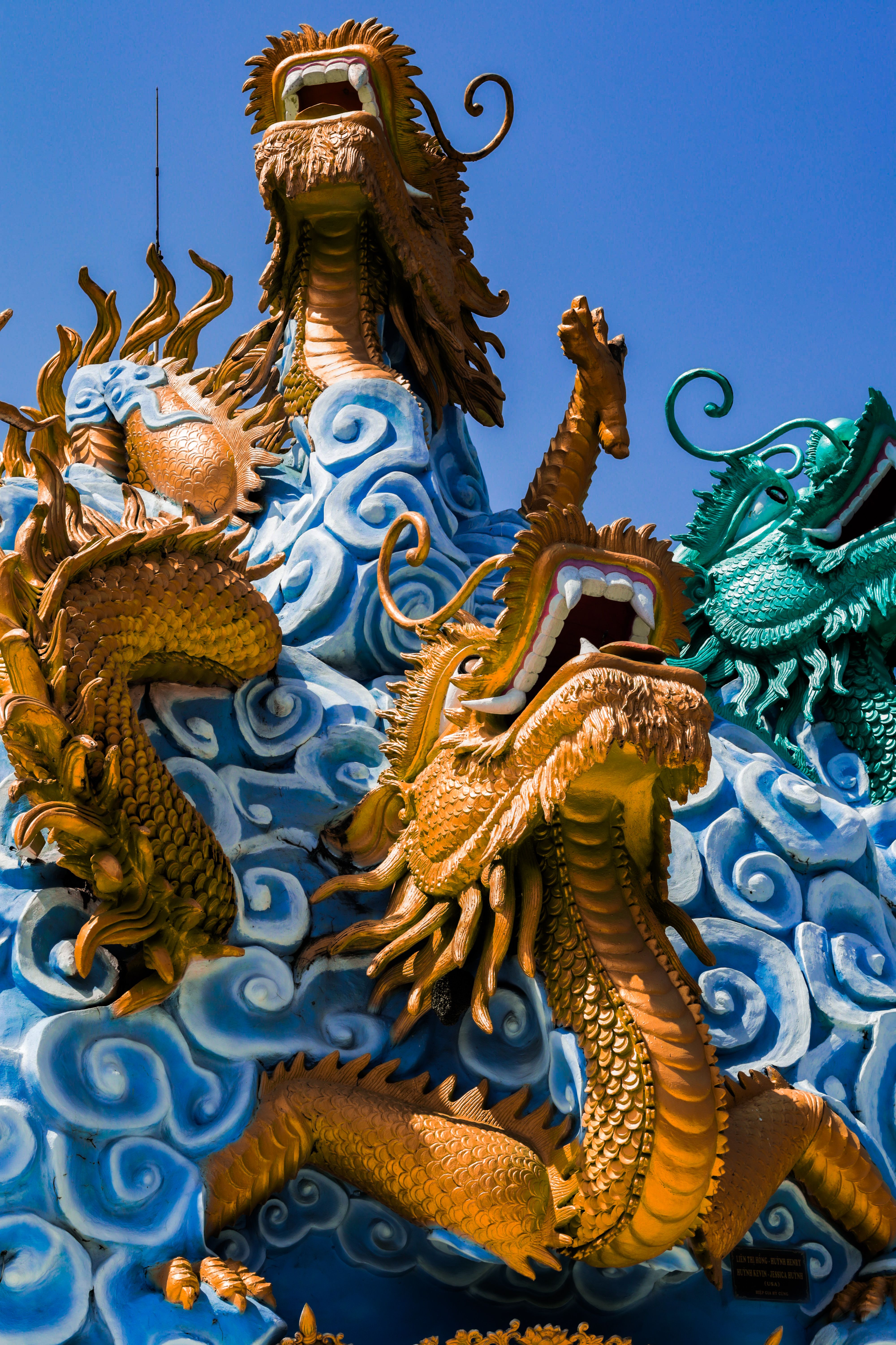 Vibrant golden and green dragon sculpture with swirling clouds under a clear blue sky.