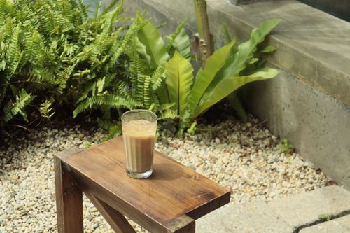 Free A refreshing iced coffee sits on a wooden table surrounded by lush garden foliage. Stock Photo