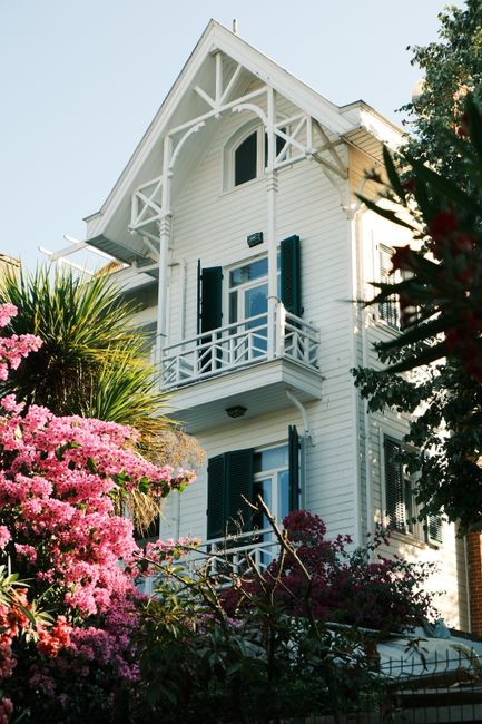 A picturesque white house surrounded by vibrant flowers under a clear summer sky in Istanbul, Turkey.