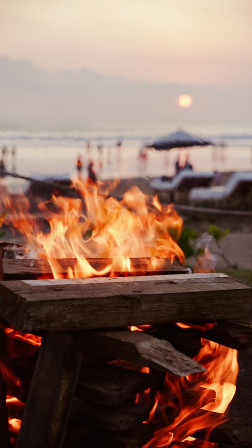 Free Relaxing beach bonfire at sunset with people enjoying the scenery in the background. Stock Photo