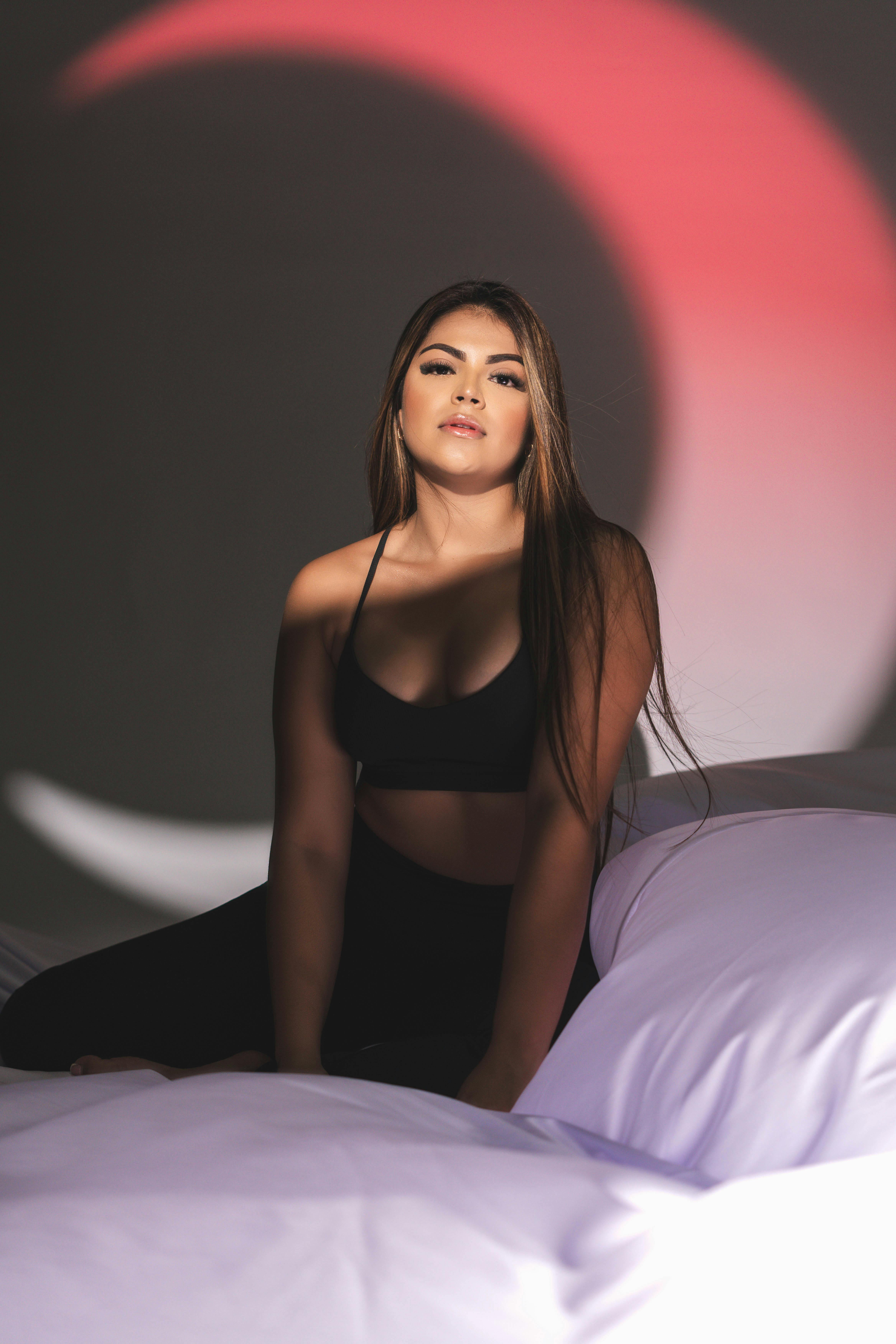 Portrait of a woman sitting on a bed in moody lighting with crescent shadow backdrop, showcasing serene elegance.