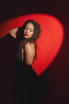 Portrait of a woman striking a pose with dramatic lighting and vibrant red background.