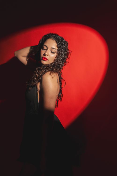Free Portrait of a woman striking a pose with dramatic lighting and vibrant red background. Stock Photo