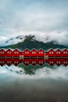 Serene view of red huts reflecting in a tranquil Norwegian fjord during autumn.