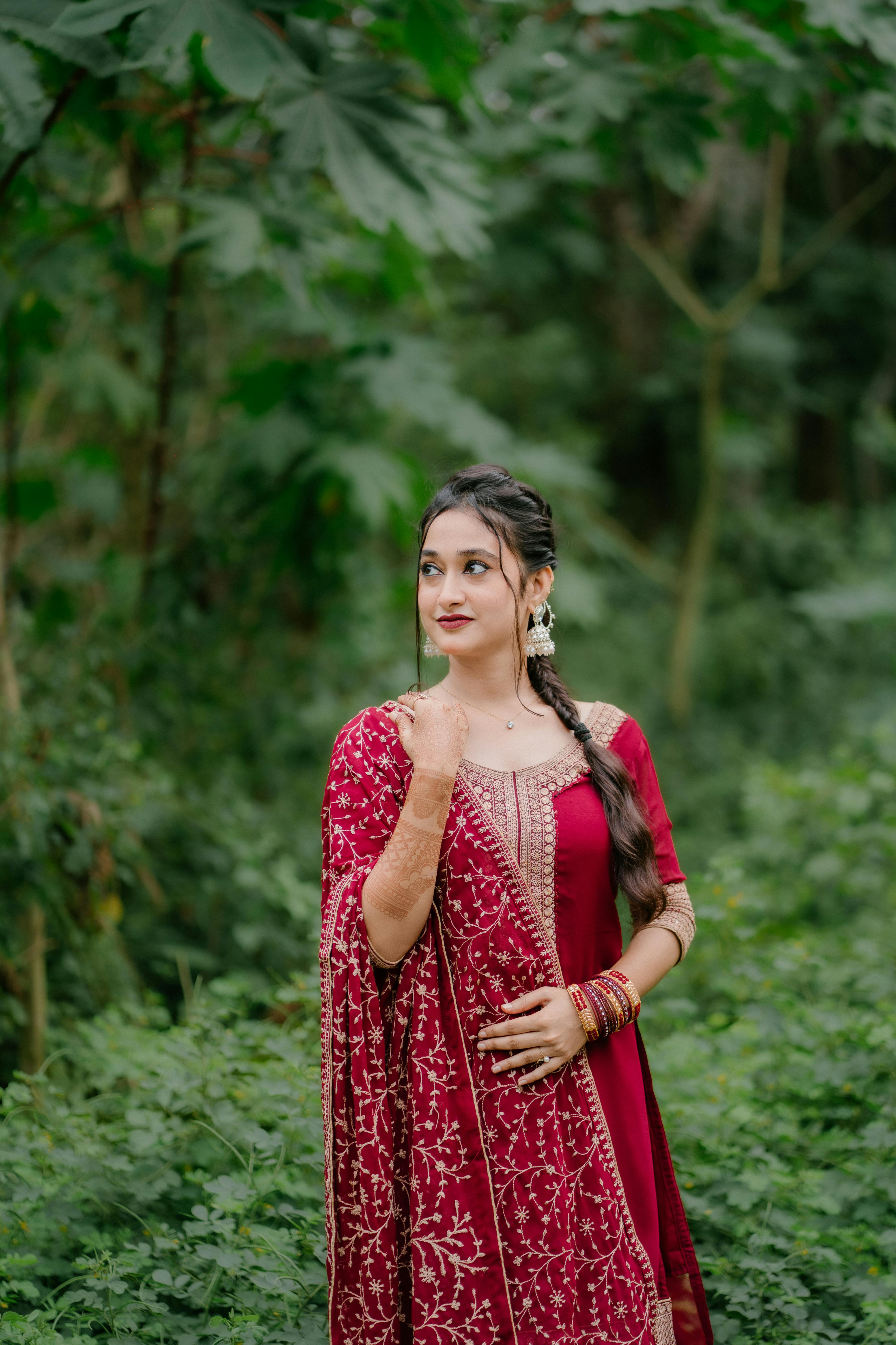 Young woman in traditional red attire posing gracefully outdoors in lush greenery.