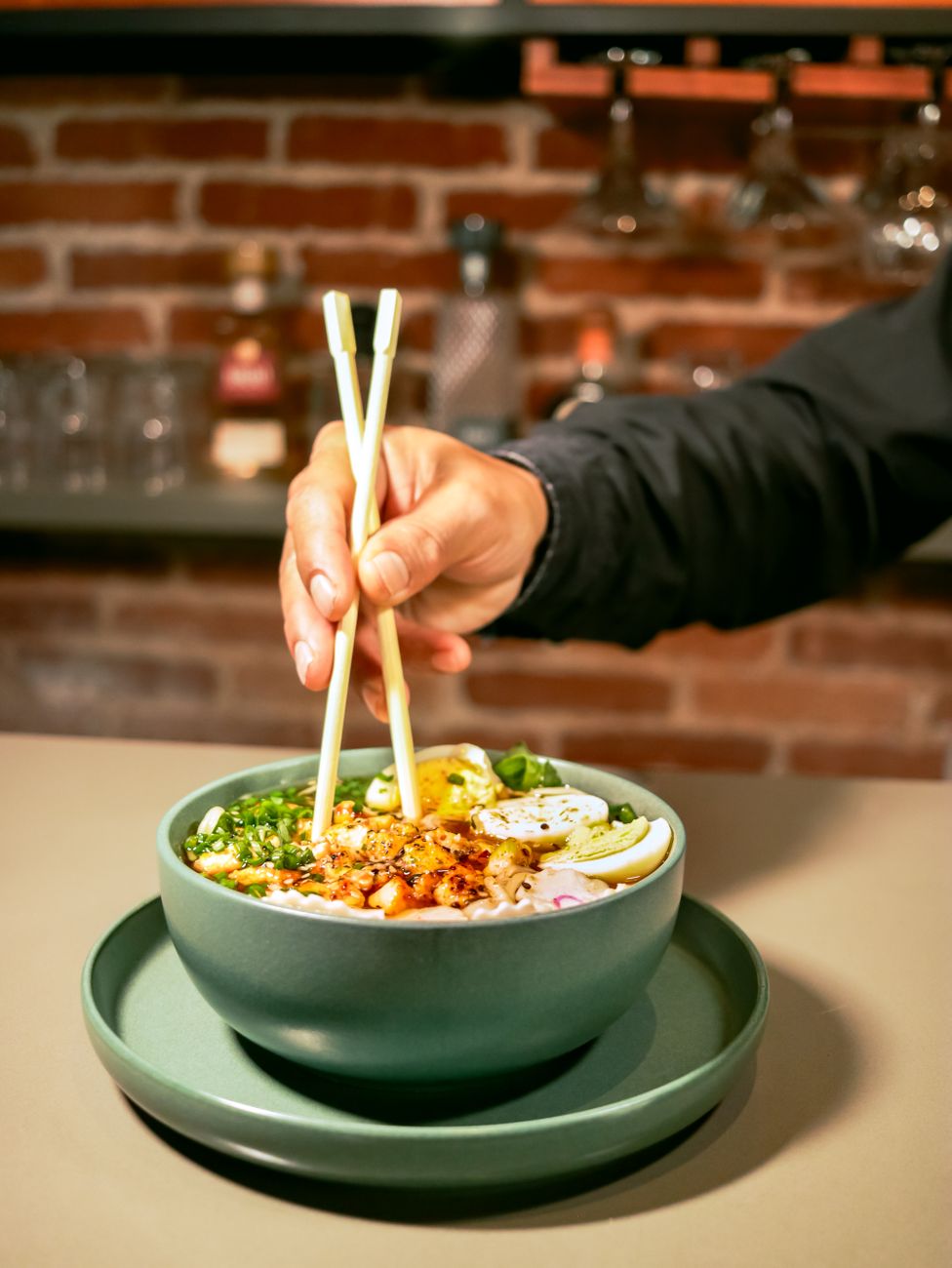 A bowl of glossy dan dan noodles coated in reddish chili oil sauce, topped with golden ground pork and bright green scallions, with chopsticks resting on the rim