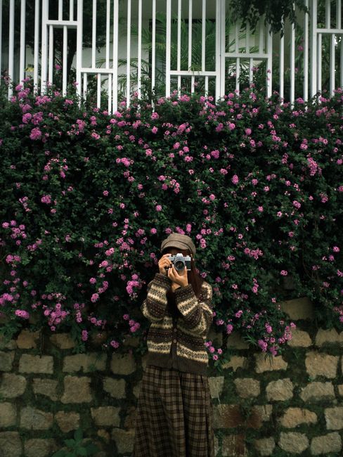 Woman with camera capturing moments in front of vibrant pink flowers.
